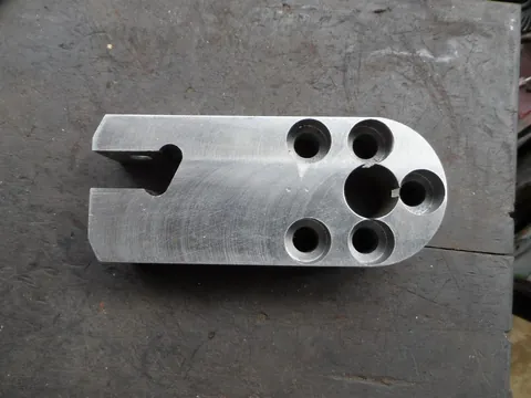 Pièce prismatique présentant plusieurs perçages et une encoche à une extrémité.
